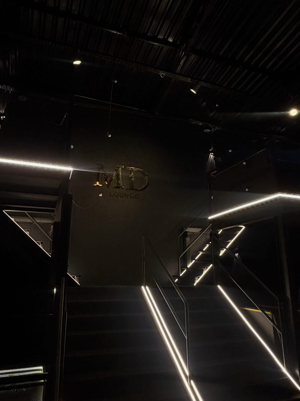 Letreiro MD Lounge no interior, com escada e corrimão em iluminação linear